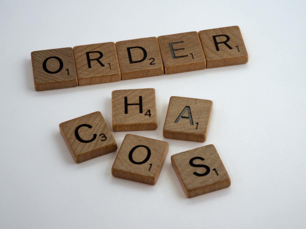 Two rows of Scrabble letter tiles. The top row is lined neatly and spells, "order." The bottom row appears to be jumbled but spells, "chaos." 